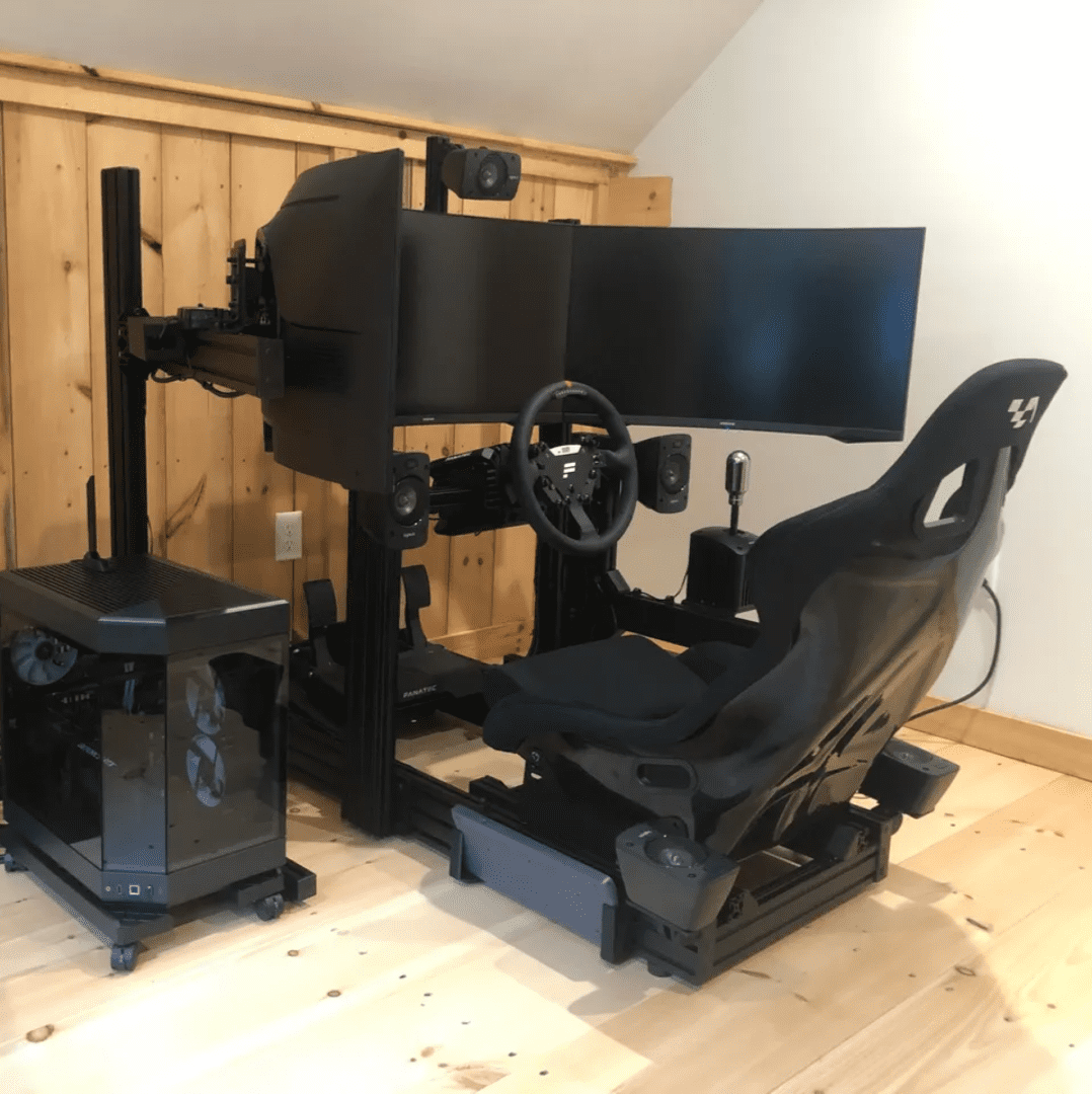 A computer desk with two monitors and a steering wheel.